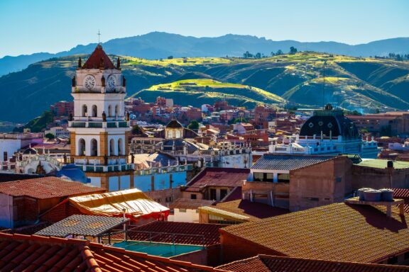 A view of building tops, a clock tower, and green hills in the distance in Sucre, Bolivia.