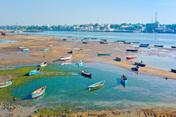 Small, colorful fishing boats sit in shallow water across from Dui, India.