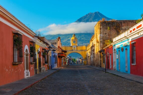 A street-level view of colorful Antigua, Guatemala with the Agua Volcano rising in the distance.