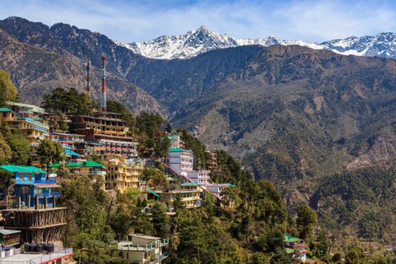 A view of buildings on a hillside with snow-covered mountains in the background.