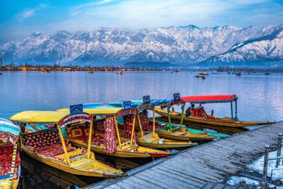 Colorful boats sit on the water, backed by snowy mountains in Dal Lake, Srinagar.