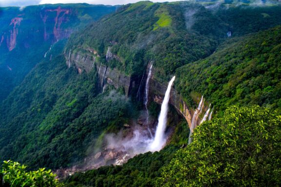 An aerial view of water cascading off a tree-covered cliff in Meghalaya.