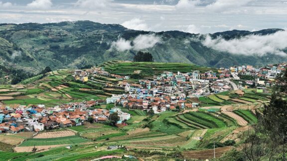 A village in Kodaikanal, Tamil Nadu sprawls across a terraced hill under a cloudy sky.