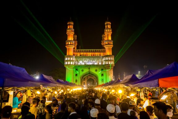 Crowds of people gather in front of the Charminar in Hyderabad at night.