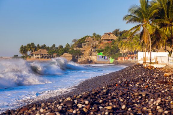 Buildings and palm trees line the rocky El Tunco Beach in El Salvador.