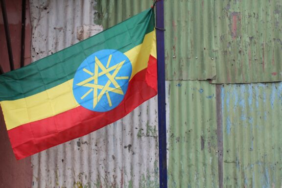 Ethiopian flag waving in front of a corrugated metal wall.