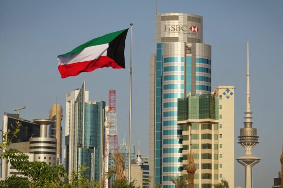 Flag of Kuwait waving in front of a skyline with modern buildings.