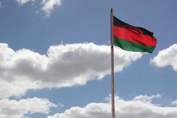 Flag of Malawi waving against a backdrop of white clouds and blue sky.