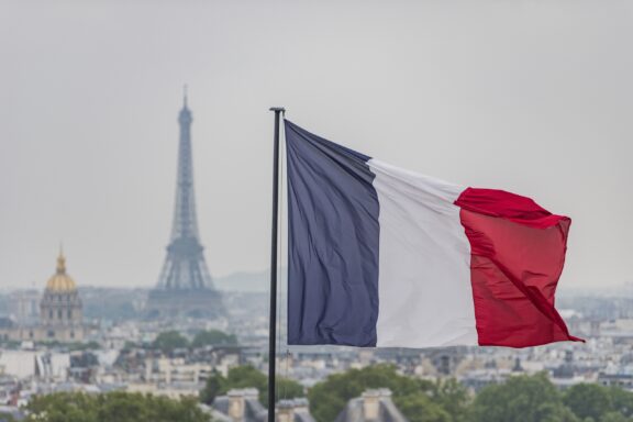 French flag waving with the Eiffel Tower and Paris skyline in the background.