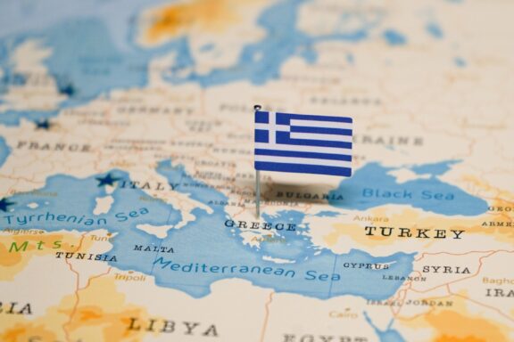 A Greek flag pin placed on Greece on a world map.