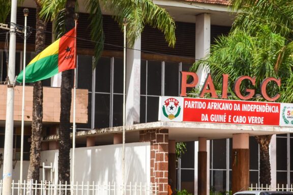 Flag of Guinea-Bissau waving in front of a building with the acronym PAIGC on it.