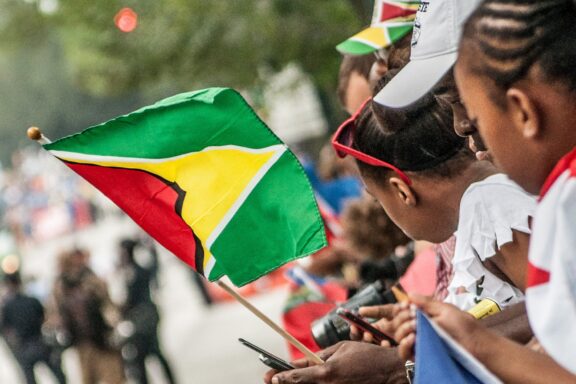 People watching a parade with someone holding the flag of Guyana.