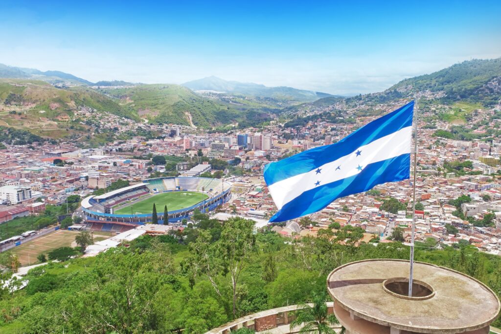 Honduras flag waving with Tegucigalpa cityscape in the background.