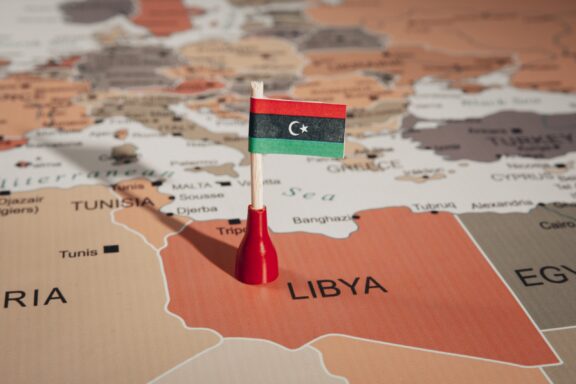 A pin with the flag of Libya placed on Libya's location on a world map.