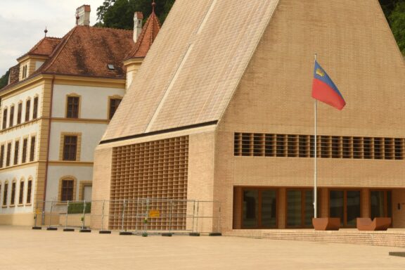 Flag of Liechtenstein flying in front of a traditional building in Vaduz.