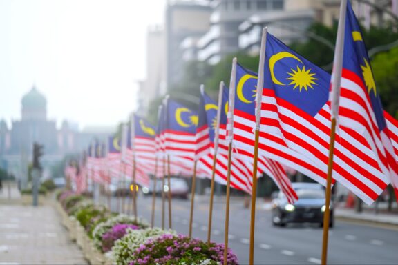 A row of Malaysian flags lining a street with buildings in the background, likely in celebration of Independence Day.