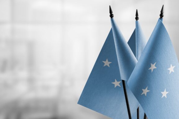 Three Micronesian flags on poles with a blurred background.