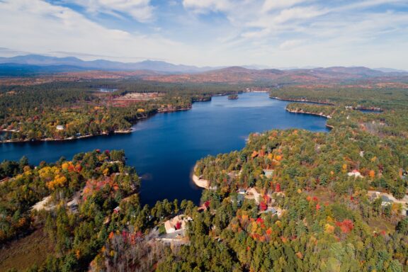 An aerial view of a large lake surrounded by trees under a blue sky.