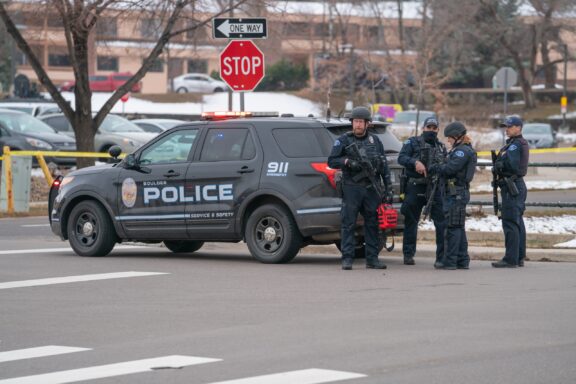 Police Officers Standing by Their Vehicle at a Roadblock Police officers with helmets and rifles stand next to a police vehicle in Boulder, Colorado.