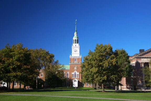 A clock tower stands tall above a grass field at Baker-Berry Library.