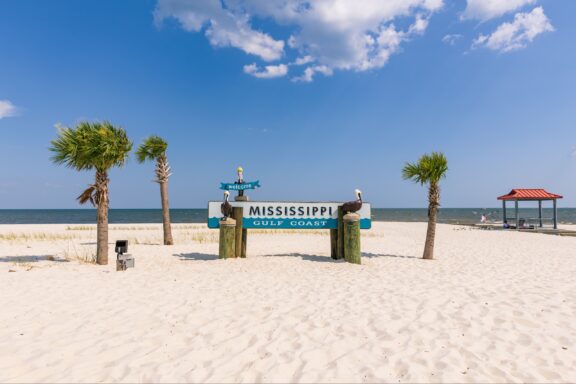 A sign on a sandy beach reads, “Mississippi Gulf Coast.”