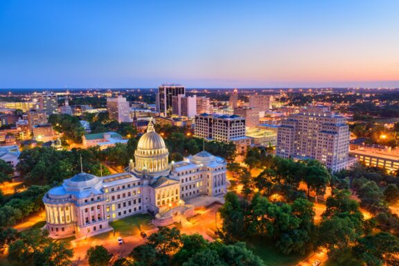 An aerial view of the Mississippi State Capitol and surrounding city at dusk.