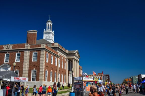 A street-level view of people and food stalls outside Truman Courthouse on a sunny day.