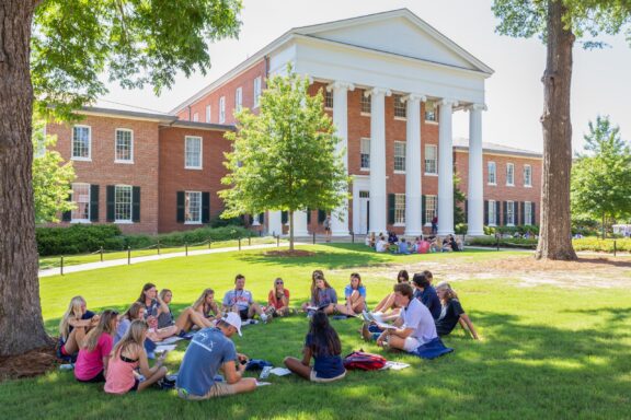 A group of students sit in the grass on the campus of the University of Mississippi.