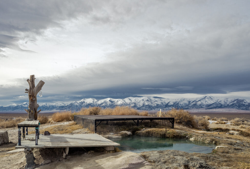 A hot spring pool in the foreground is backed by the distant, snow-capped Toiyabe Range in Lander County.