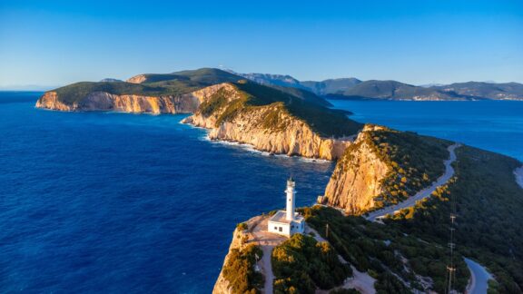 An aerial view of a lighthouse on top of a cliff, surrounded by water at sunset.