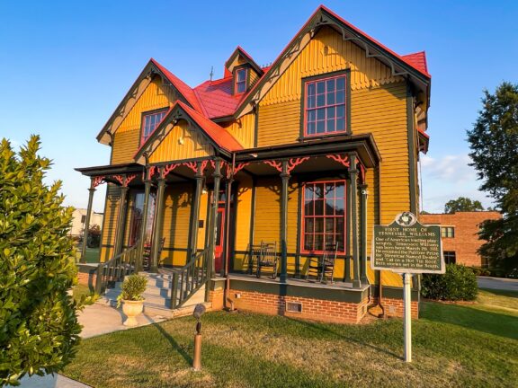 A low-angle view of a yellow house with green trim and a red roof in Columbus, Mississippi.