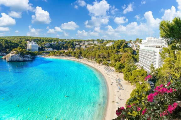 An aerial view of turquoise waters and a white sand beach on Menorca, Spain.