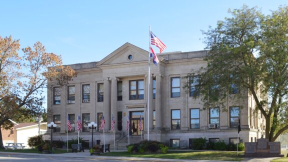 American flags fly in front of the façade of the Mercer County Courthouse on a sunny day in Princeton, Missouri.