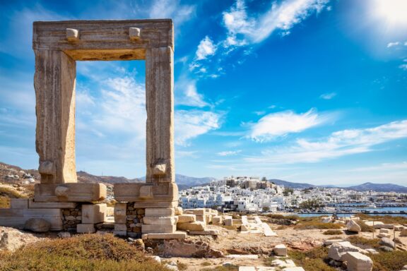 A small town of white buildings is in the background, and the stone Portara stands in the foreground on the Mediterranean island of Naxos.