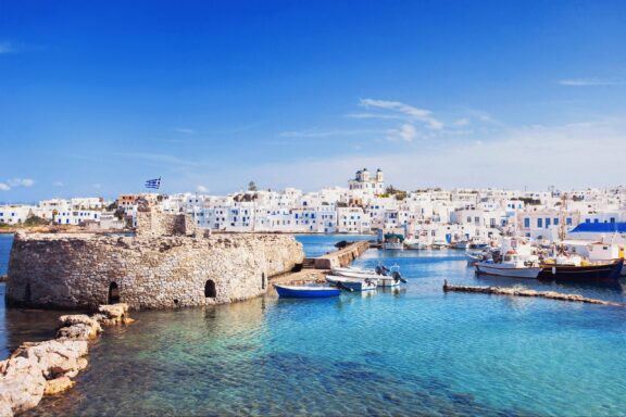 Boats and white buildings meet blue waters in Paros, Greece.