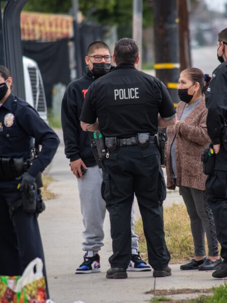 Police Officers Engaging with Civilians During a Stop in Northridge, California A police officer questions two people wearing face masks on the street.