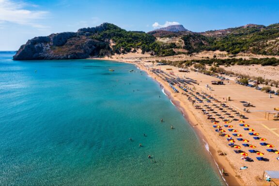 An aerial view of many rows of umbrellas and chairs on a sandy beach on the island of Rhodes.