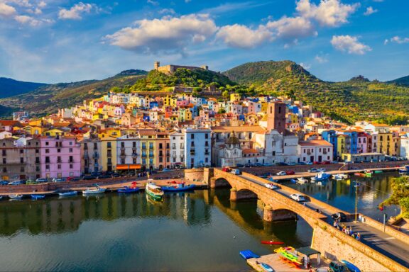 An aerial view of colorful buildings and a bridge next to green hills in Bosa, Sardinia.