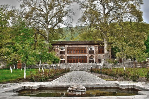 The facade of the Palace of Shaki Khans is framed by two very tall trees. 