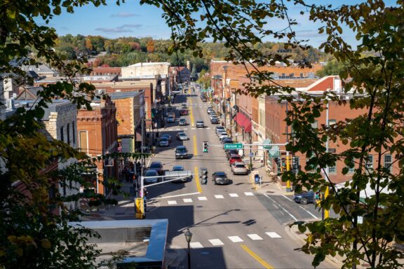 Downtown Stillwater, Minnesota can be seen from a hill through trees on a sunny day.