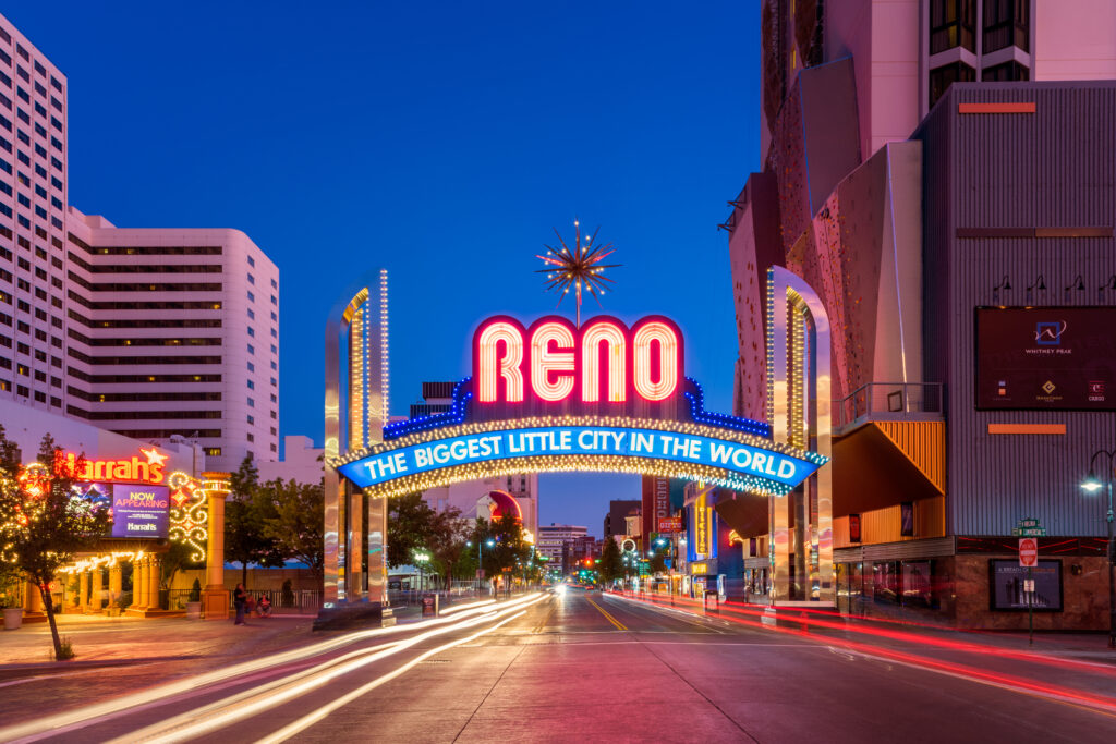 A neon sign over a road reads, “Reno” and, “The Biggest Little City in the World.”