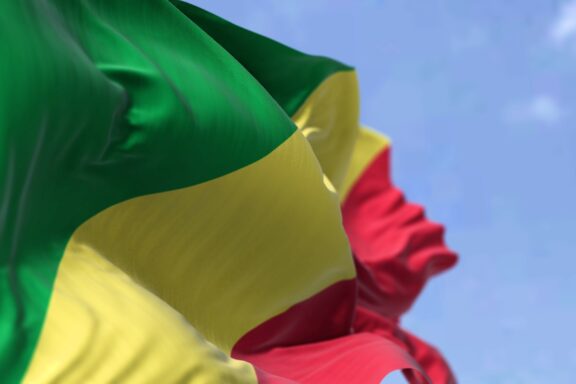 A close-up of the Republic of the Congo flag fluttering in the wind, with a clear blue sky in the background.