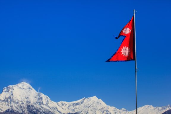 Nepalese flag waving in front of the snow-covered Himalayan mountains under a clear blue sky.