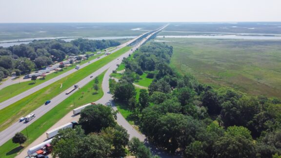 An aerial view of a highway, trees, and the Pascagoula River Bridge in the distance.