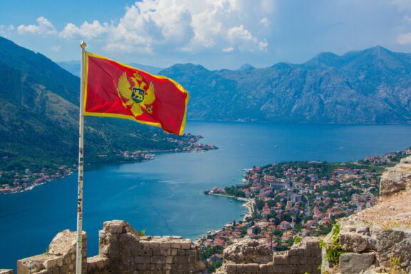 Montenegro flag waving with Kotor Bay and mountains in the background.