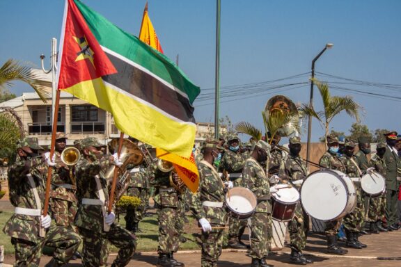 Soldiers in camouflage marching with the Mozambique flag and a brass band in a parade.