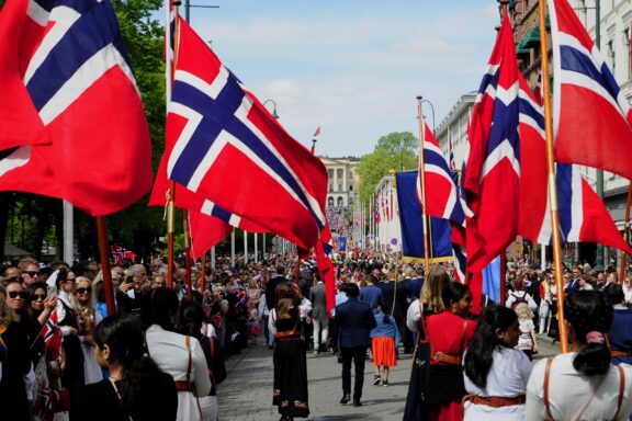 Crowd of people celebrating with Norwegian flags on a street, likely during a national holiday or parade.