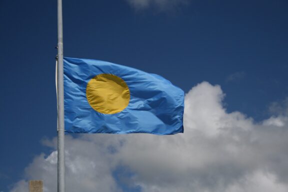 Flag of Palau waving against a cloudy sky.