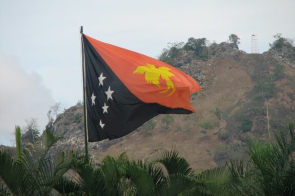 Flag of Papua New Guinea waving with a mountainous background.