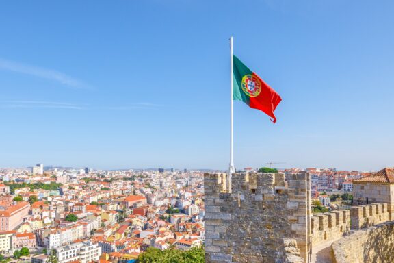 Portuguese flag waving above the cityscape of Lisbon under a clear blue sky.